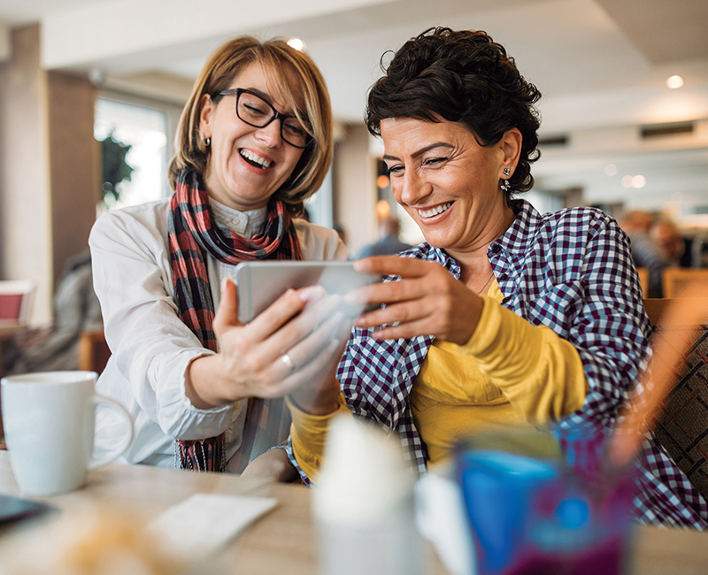 Two women look a something funny on a phone while having coffee together