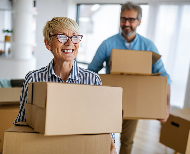 A middle aged couple smiles as they move boxes into their new home.