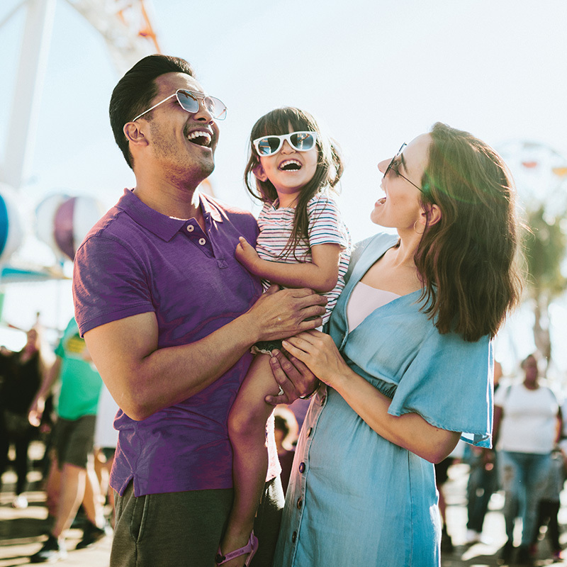 A family hugs their little girl while at an amusement park